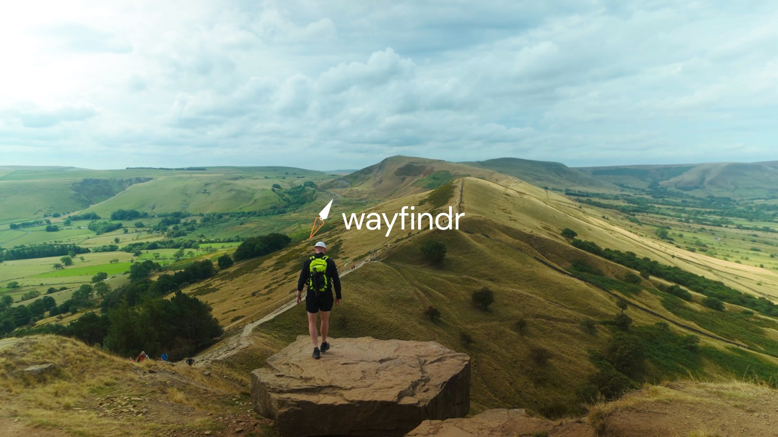 A walker on a hilltop path with the Wayfindr logo
